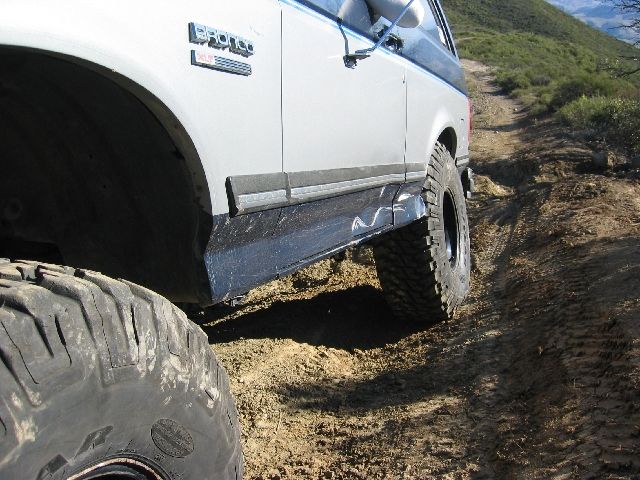 White Ford Bronco lower side on rutted dirt off-road trail with large mud tires