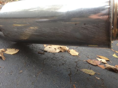 1996 Ford Bronco - A close-up view of a damaged chrome exhaust pipe lying on a cracked asphalt surface with scattered autumn leaves.