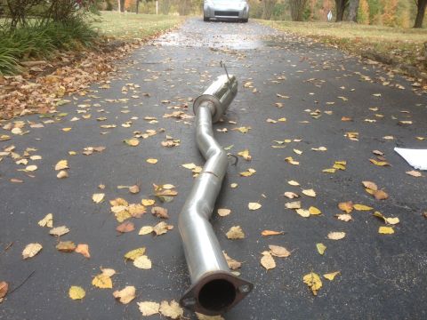1996 Ford Bronco - An aftermarket exhaust pipe lies on a leaf-strewn driveway, with a silver car parked in the background.