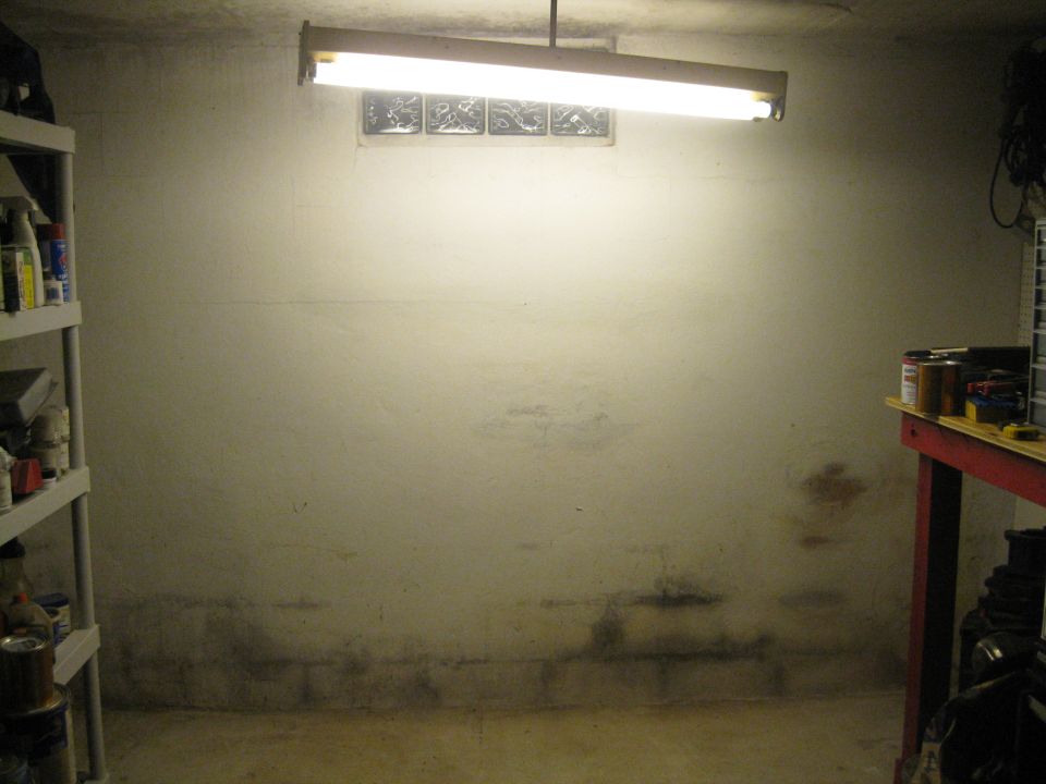 Basement with concrete floor and walls, fluorescent light, window, shelving unit, and workbench