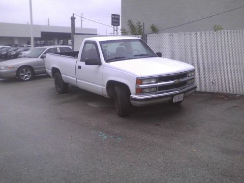 2003 Ford Crown Victoria - White pickup truck parked next to a silver sedan in a lot.
