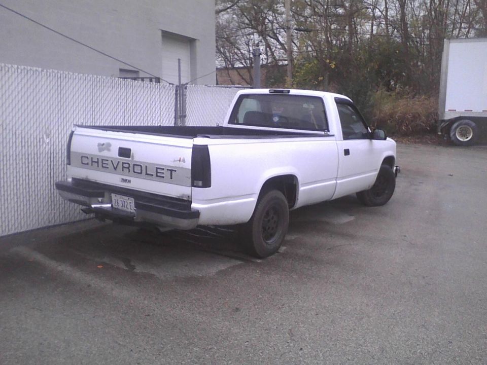 White Chevrolet pickup truck parked next to a fence and a box truck