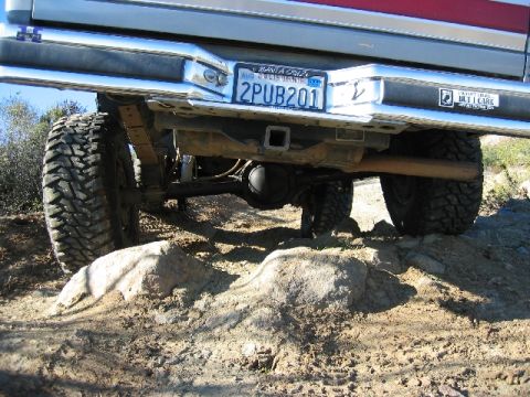 1989 Ford Bronco - The undercarriage of a vehicle with large off-road tires navigates a rocky terrain.