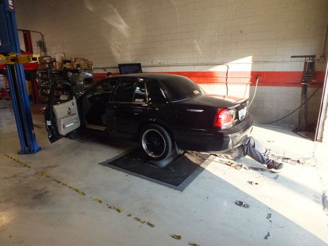 2003 Ford Crown Victoria - Black Crown Victoria strapped to a dyno in a garage, laptop on a cart and a mechanic beneath it