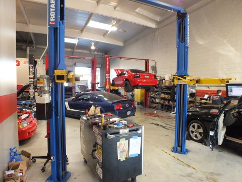 2003 Ford Crown Victoria - Tuning shop floor showing two blue lifts, a red coupe raised and dark cars in adjacent service bays