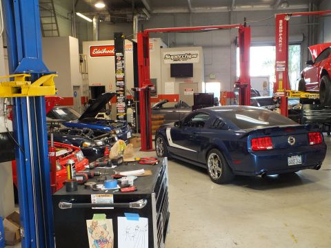 2003 Ford Crown Victoria - Dark blue Mustang GT parked in a tuning bay next to an open engine bay and scattered tools