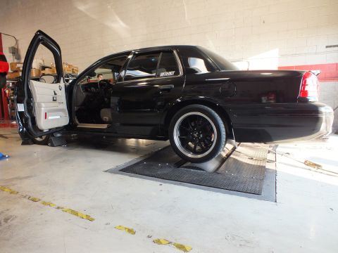 2003 Ford Crown Victoria - Side view of a black full-size sedan staged on dyno rollers with door open and dark alloy wheels