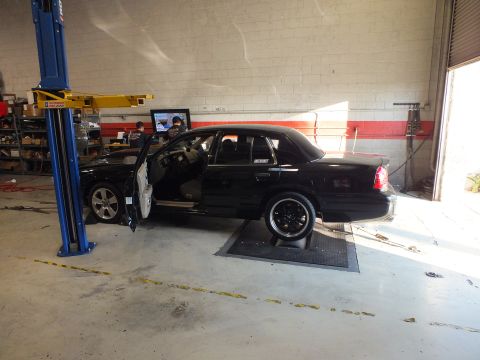 2003 Ford Crown Victoria - Black sedan positioned on dyno rollers near a blue post lift with a tuning monitor in view