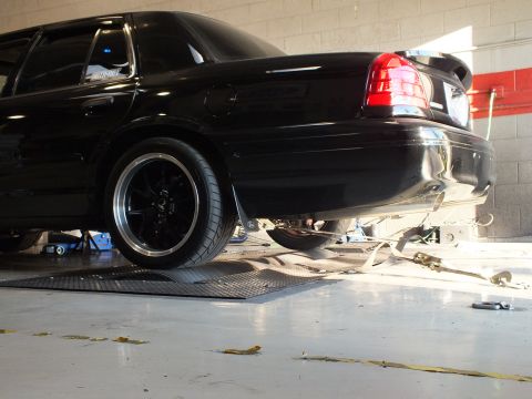 2003 Ford Crown Victoria - Tight low rear-quarter view of a black sedan rear wheel and tail light while on dyno rollers