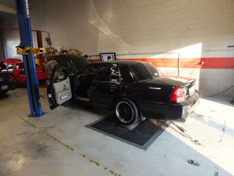 2003 Ford Crown Victoria - Black full-size sedan staged on dyno rollers, door open, monitor and blue lift visible behind