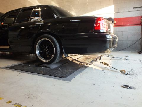 2003 Ford Crown Victoria - Low angle of a black sedan rear quarter on dyno rollers with black wheel and trailing exhaust