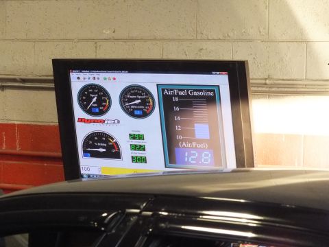2003 Ford Crown Victoria - Black sedan on dyno rollers with hood raised and a technician lying beneath the rear of the car