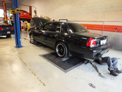 2003 Ford Crown Victoria - Young man in a gray tee reads a printout while walking through a shop with lifts and parked cars
