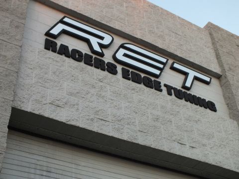 2003 Ford Crown Victoria - Mounted RET logo and Racers Edge Tuning name on a beige cinder-block shop facade.