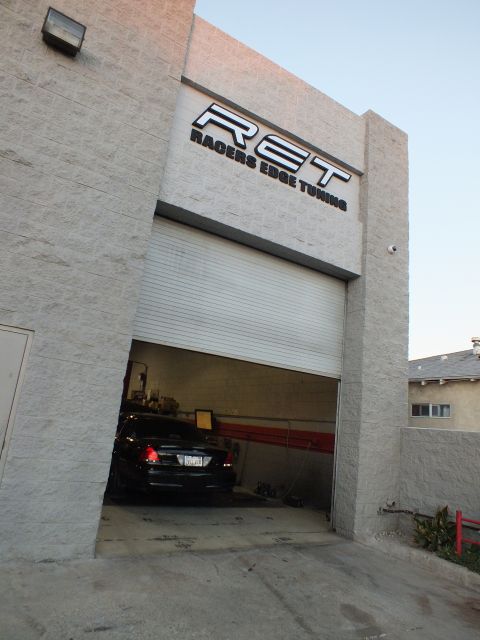 2003 Ford Crown Victoria - Tall block storefront with RET sign above an open garage door; dark sedan parked in the lit bay.