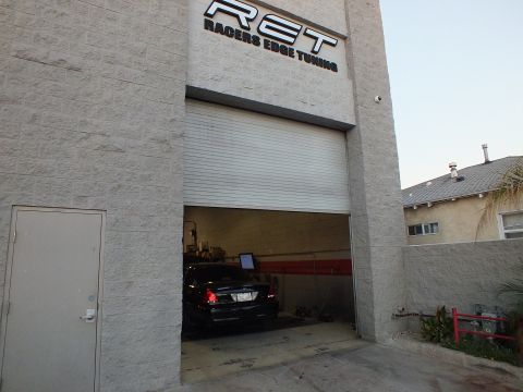 2003 Ford Crown Victoria - RET shop bay open to a black sedan and monitor inside, neighboring house visible at right.