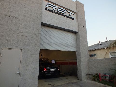 2003 Ford Crown Victoria - RET signage over an open shop door, black sedan and tools inside, palm and fence beside building.