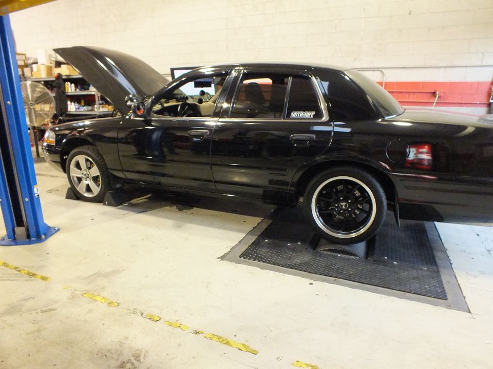 Black Ford Crown Victoria side profile with hood open on dyno inside tuning shop