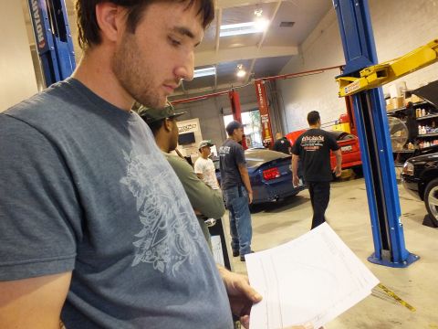 2003 Ford Crown Victoria - Close shot of a man holding a dyno chart, with crew, lifts and a dark car in the workshop behind.