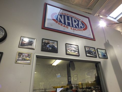 2003 Ford Crown Victoria - NHRA Drag Racing sign mounted over framed photographs and a window into the shop office.