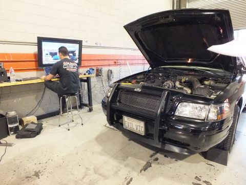 2003 Ford Crown Victoria - Tech at a laptop tunes a black sedan with push bar and large intercooler, EVIL VIC front plate.