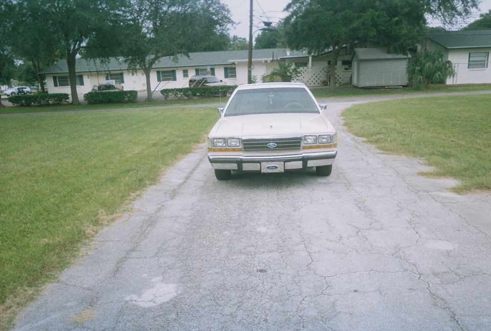 Front view of a white Ford Crown Victoria parked on a cracked driveway