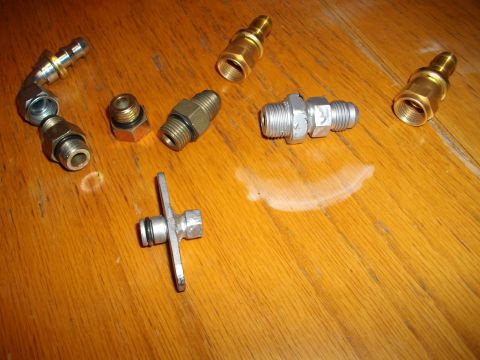 1989 Ford Probe - A collection of various metal fittings and adapters are laid out on a wooden surface.