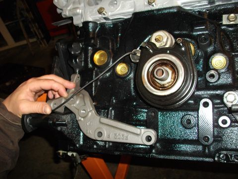 1989 Ford Probe - Close-up of an engine block with a hand manipulating a metal bracket, showing part numbers and an oil filter housing.