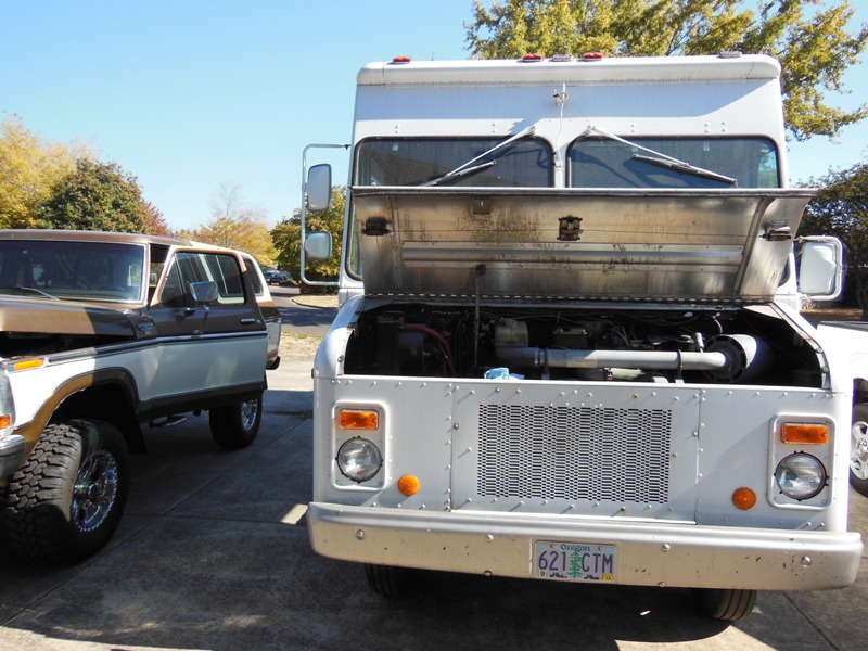 White delivery truck front view, hood open, showing engine. License plate 621 CTM
