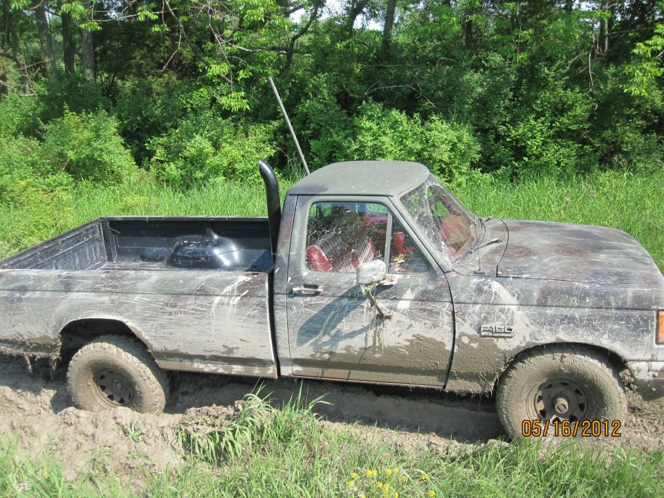 Mud-covered 1987 Ford F-150 stuck in mud, side view. Black exhaust stack visible