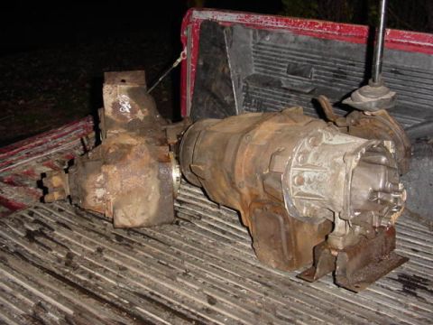 1992 Ford Bronco - A grimy manual transmission bolted to a transfer case, pulled from a truck and sitting in the ribbed bed of a red pickup at night with the…