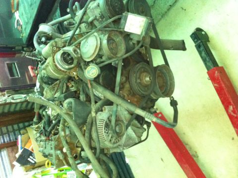 1986 Ford Bronco - This engine assembly is suspended by a red engine hoist, showing a complex arrangement of belts and pulleys.