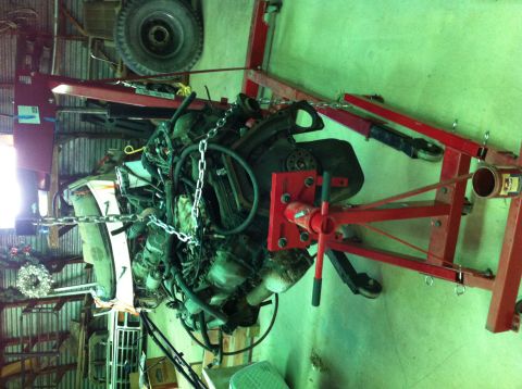 1986 Ford Bronco - Engine assembly is suspended by a red engine hoist, with chains and hoses visible.