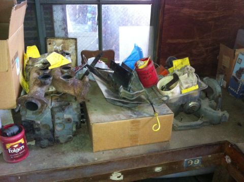 1986 Ford Bronco - Engine parts and storage boxes are piled on a workbench in a cluttered garage.