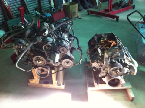 1986 Ford Bronco - Two V8 engines are displayed on wooden stands in a workshop environment.