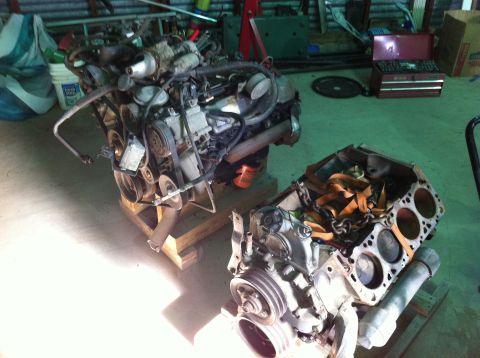 1986 Ford Bronco - Two V8 engines are visible in a garage setting, one appears to be a bare block.