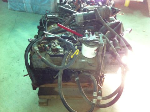 1986 Ford Bronco - Engine assembly with various components and hoses attached, resting on wooden pallets.