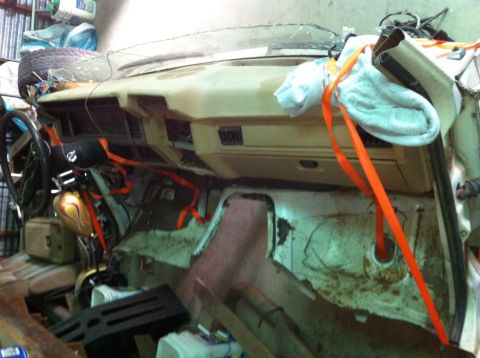 1986 Ford Bronco - The interior of a 1986 Ford Bronco shows a tan dashboard and steering wheel, secured with orange straps.