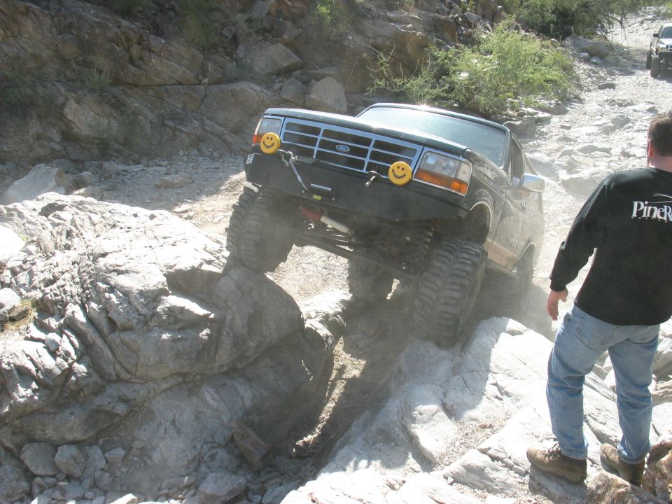 Lifted dark Ford Bronco climbing a rock ledge with front wheel in the air