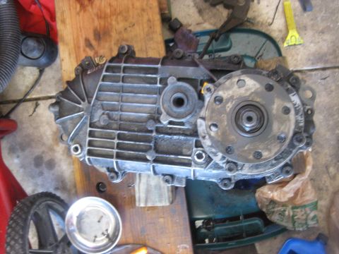 1994 Ford Bronco - A transfer case component is shown disassembled on a workbench, with tools and a plastic bag nearby.