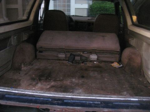 1994 Ford Bronco - The cargo area of an SUV shows a folded rear seat and a suitcase, with a "Supermotors.net" watermark at the bottom.