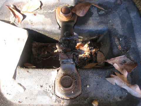 1994 Ford Bronco - Close-up of a rusted metal linkage part, partially covered by fallen leaves.