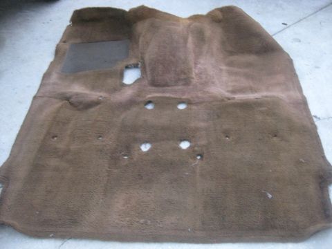 1994 Ford Bronco - A brown carpet floor mat for a 1994 Ford Bronco is shown laid out on a concrete surface. The carpet has several circular cutouts and a rect…