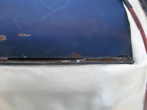 1994 Ford Bronco - Close-up of a blue metal panel showing significant rust damage along its lower edge.