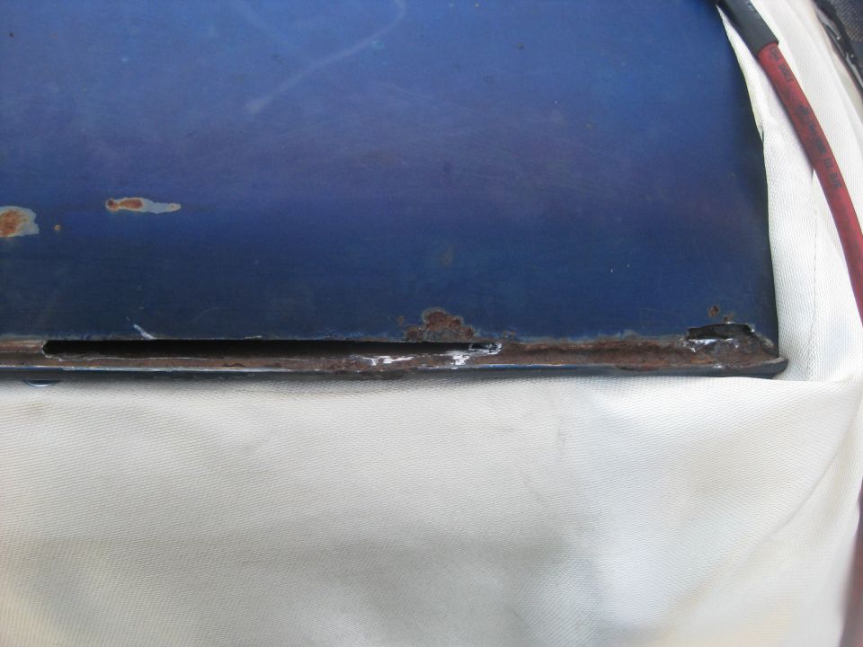 Blue metal panel with rust along the bottom edge and a small cutout