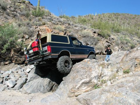 1994 Ford Bronco - A modified Ford Bronco tackles a challenging rocky trail under a clear blue sky.