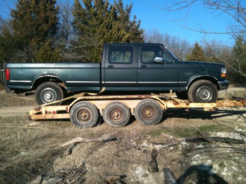 1986 Ford Bronco - A dark green 1992 Ford F-Series truck is transported on a rusty triple-axle trailer.