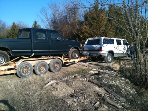 1986 Ford Bronco - A dark green Ford F-Series truck is loaded onto a trailer, with a white SUV positioned behind it.