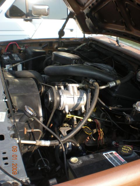 1986 Ford Bronco - The engine compartment of a vehicle is shown, with various hoses, belts, and the AC compressor clearly visible.