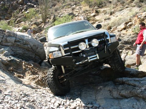 1994 Ford Bronco - This modified truck is tackling a challenging off-road trail with large rocks and steep inclines.